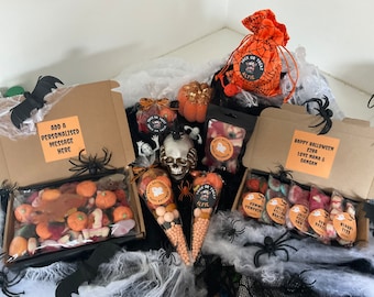 May include: A Halloween gift box filled with various candies, including gummy eyeballs, pumpkin-shaped candies, and a cone of candy. The box is decorated with a spider web and a bat. The box also includes a personalized message, a small bag of candy, and a skull-shaped candy dish.
