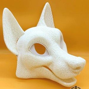 Puede incluir: Una máscara canina blanca, texturizada, impresa en 3D, con orejas grandes y aberturas para los ojos. La máscara tiene una superficie porosa detallada y está sobre un fondo amarillo. El texto "FURRY FACTORY" es visible en la parte inferior.