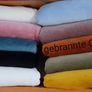 Może przedstawiać: Stosik próbek tkanin w różnych kolorach, w tym białym, różowym, niebieskim, czarnym, pomarańczowym, zielonym i żółtym. Na jednej z próbek widoczny jest tekst "gebrannte Orange".