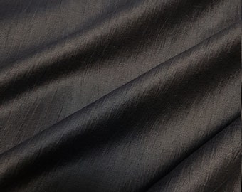 May include: Close-up of a dark charcoal-colored fabric with a subtle sheen. The material is draped, creating soft folds and shadows. The texture appears slightly textured, suggesting a woven or textured textile.
