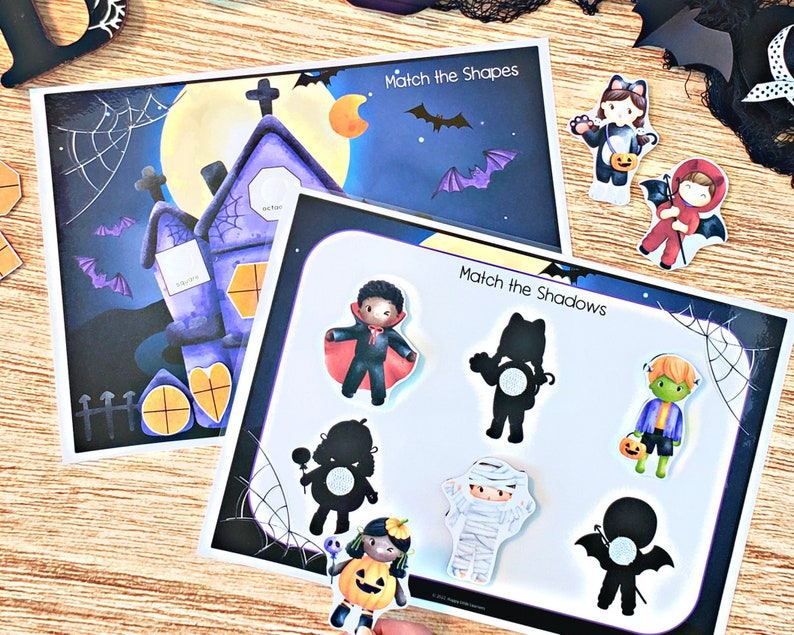 May include: Two Halloween-themed matching games. The first game is called "Match the Shapes" and features a purple house with a yellow moon and bats. The second game is called "Match the Shadows" and features a variety of Halloween characters, including a vampire, a mummy, a witch, and a ghost.