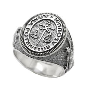 Puede incluir: Un anillo de plata con un diseño ovalado en relieve que presenta una espada y una balanza, rodeado de la frase latina "ARMA AEQUUM POTENTIUS".
