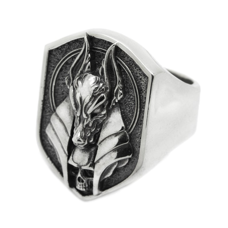 May include: A silver ring with a detailed design of an Anubis head with a skull underneath. The ring is shaped like a shield.