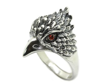 Puede incluir: Anillo de plata con un diseño detallado de cabeza de águila. El ojo del águila es una pequeña gema roja. El anillo tiene un acabado pulido y una banda que se estrecha hacia la parte posterior. Una joya única.