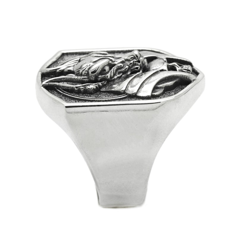 May include: A silver ring with a detailed dragon design on the face. The ring has a octagonal shape and a wide band.
