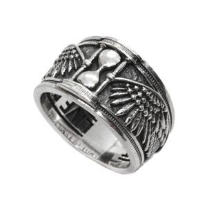 Puede incluir: Un anillo de plata con un diseño de reloj de arena y alas. El anillo es ancho y tiene una superficie texturizada.