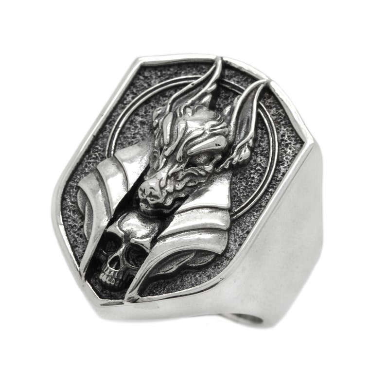 May include: A silver ring with a detailed design of a wolf's head with a skull underneath. The ring is shaped like a shield.