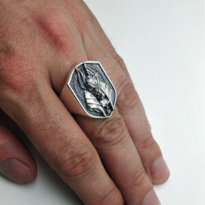 May include: A silver ring with a detailed design of a wolf's head. The ring is on a person's finger.
