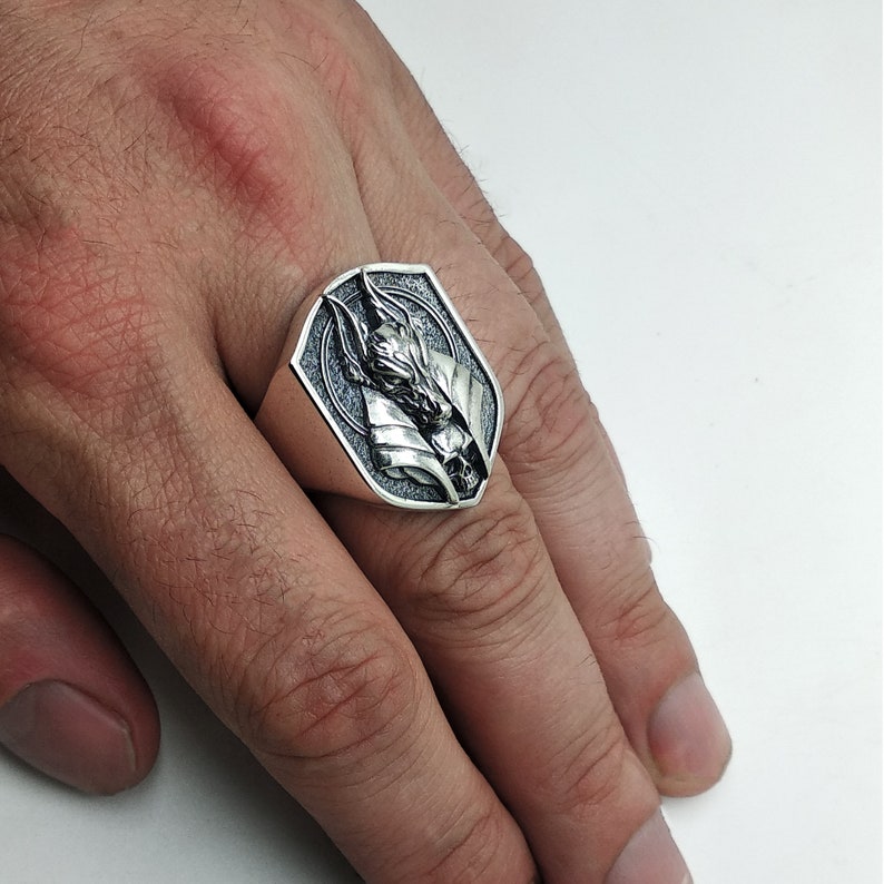 May include: A silver ring with a detailed design of a wolf's head. The ring is on a person's finger.