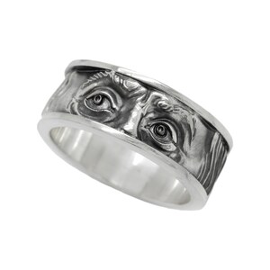Könnte beinhalten: Ein silberner Ring mit einem detaillierten Design von zwei Augen auf der Band.