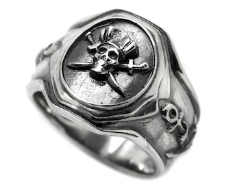 May include: A silver ring with a skull and crossbones design. The skull is wearing a pirate hat and the crossbones are swords. The ring also has an anchor design on the side.