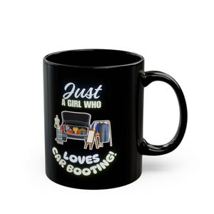 Pode incluir: Caneca de cerâmica preta com a frase branca "Just a girl who loves car booting!". O design inclui uma mala de carro cheia de objetos e roupas num cabide. A caneca tem uma pega curva.