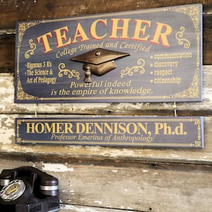 May include: Two wooden signs with gold lettering. The top sign reads "TEACHER College Trained and Certified" with a graduation cap image and a list of qualities. The bottom sign reads "HOMER DENNISON, Ph.d. Professor Emeritus of Anthropology".