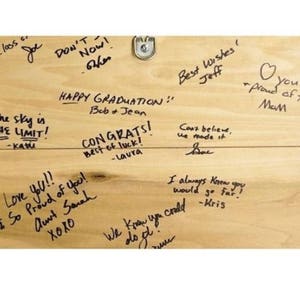 May include: A wooden sign with handwritten messages of congratulations and well wishes. The sign includes the text "Happy Graduation", "Congrats", "Best of Luck", "Love you", "Proud of you", "The sky is the limit", "Best Wishes", "Can't believe we made it", "I always knew you would go far", "We knew you could do it", "You proud of you".