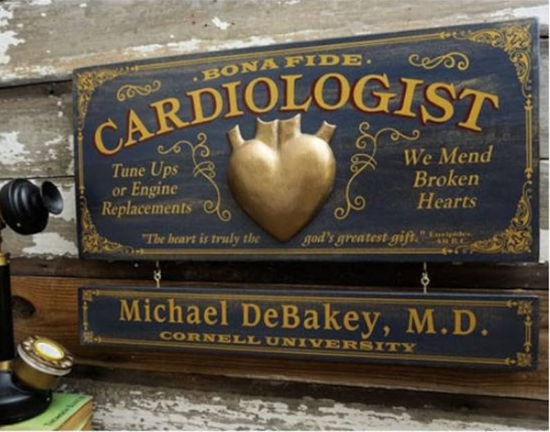 K&ouml;nnte beinhalten: Ein Vintage-Holzschild mit dem Text "Bona Fide Cardiologist" in goldenen Buchstaben. Das Schild zeigt ein goldenes Herz mit dem Text "We Mend Broken Hearts" und "Tune Ups or Engine Replacements". Das Schild enth&auml;lt auch den Text "The heart is truly the god's greatest gift." und "Michael DeBakey, M.D. Cornell University".