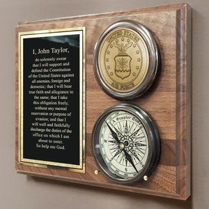May include: A wooden plaque with a gold plaque with the text "I, John Taylor, do solemnly swear that I will support and defend the Constitution of the United States against all enemies, foreign and domestic; that I will bear true faith and allegiance to the same; that I take this obligation freely, without any mental reservation or purpose of evasion; and that I will well and faithfully discharge the duties of the office on which I am about to enter. So help me God."  A gold and silver United States Air Force emblem and a compass with the text "A Simpler Time" are also on the plaque.