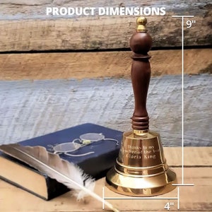 May include: A brass bell with a dark wood handle, measuring 9 inches tall and 4 inches wide. The bell has an engraved inscription that reads "Thanks to my teacher of the year Gloria King." A book and quill are in the background.