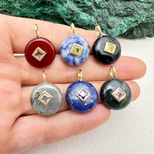May include: Six gemstone pendants with gold-coloured bails. The round pendants display colours such as red, blue, black, grey, and dark blue. Each pendant has a square gemstone in the centre, adding a touch of elegance.