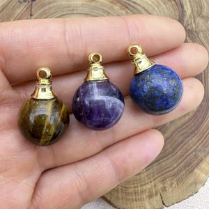 Puede incluir: Tres colgantes de tono dorado con esferas de piedras preciosas diferentes. Los colgantes presentan un ojo de tigre, una amatista y un lapislázuli.