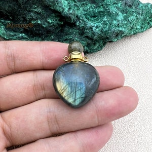 May include: A heart-shaped labradorite stone pendant with a gold-toned metal cap and a loop for attaching a chain. The stone has a dark blue, green, and gold iridescent sheen.