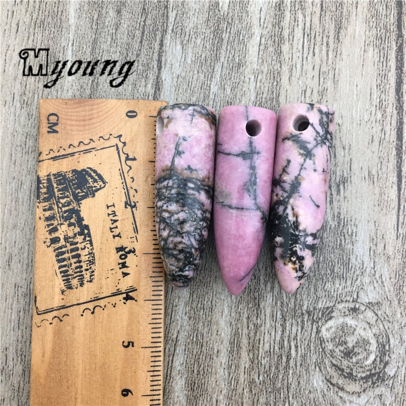 May include: Three pink and black gemstone pendants with a hole drilled through the top. The pendants are about 4 cm long.