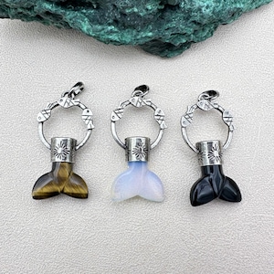 May include: Three silver pendants with fish designs and different colored gemstone tails. The tails are tiger's eye, white, and black.