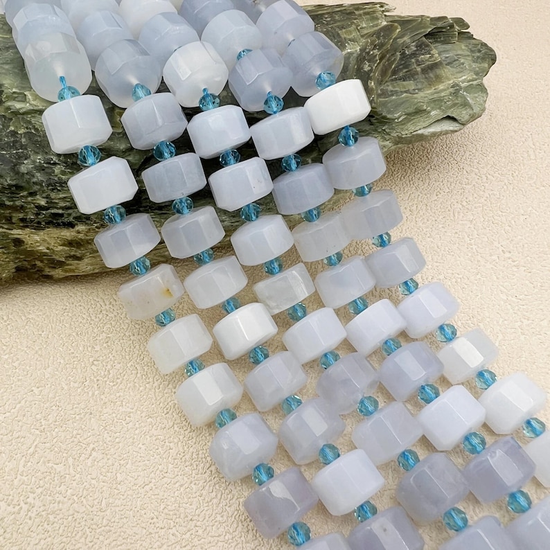 May include: A strand of light blue chalcedony beads with faceted accents. The beads are square shaped and have a smooth, polished finish.