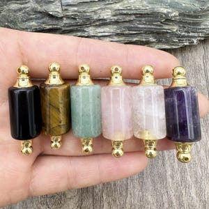 Pode incluir: Seis rolhas de garrafa de cristal com pedras de diferentes cores, coroadas com tampas douradas. As rolhas estão dispostas em fila, da esquerda para a direita: preto, olho de tigre, verde, quartzo rosa, quartzo transparente e ametista.
