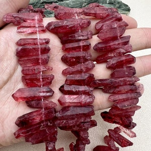 May include: A strand of red quartz crystal points, also known as red phantom quartz, with a natural, raw, and rough texture. The crystals are faceted and have a deep red color.