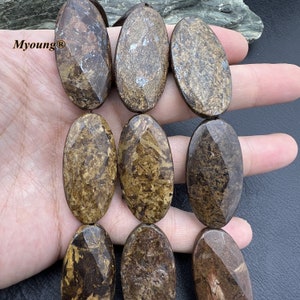 Könnte beinhalten: Eine Kette aus braunen und goldenen ovalen Edelsteinperlen. Die Perlen haben ein gesprenkeltes Muster und eine facettierte Oberfläche.