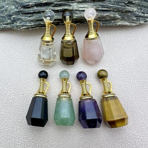 Pode incluir: Conjunto de dez pequenas garrafas decorativas feitas de várias pedras preciosas, incluindo quartzo transparente, quartzo fumado, quartzo rosa, obsidiana negra, aventurina verde, ametista e olho de tigre. Cada garrafa tem uma rolha dourada e uma alça dourada.