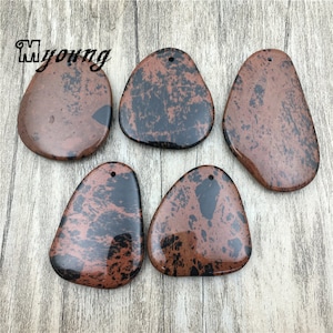 Puede incluir: Cinco colgantes de piedra moteados de marr&oacute;n y negro con un agujero en la parte superior para colgar. Las piedras tienen una forma irregular y un acabado liso y pulido.
