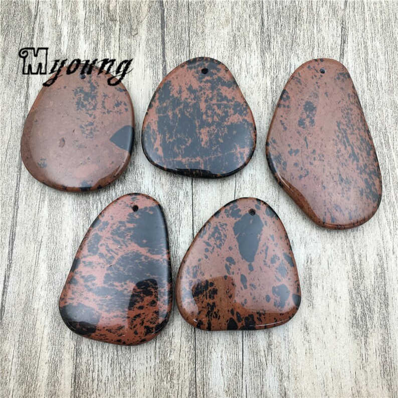 Puede incluir: Cinco colgantes de piedra moteados de marr&oacute;n y negro con un agujero en la parte superior para colgar. Las piedras tienen una forma irregular y un acabado liso y pulido.