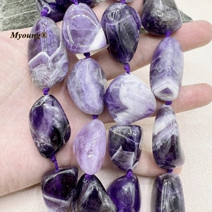 Puede incluir: Una hebra de cuentas de piedra preciosa de amatista púrpura y blanca. Las cuentas son lisas y pulidas, y tienen una forma natural y orgánica. Las cuentas están enhebradas en un cordón morado.