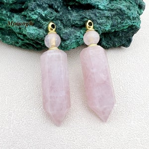 May include: Two pink rose quartz crystal bottle stoppers with gold caps. The stoppers are shaped like a long, thin, pointed rectangle.