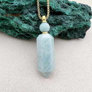 May include: A gold chain necklace with a light blue crystal pendant shaped like a bottle. The bottle has a gold top and a gold bead at the top of the bottle.
