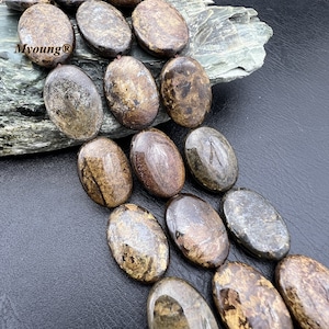 Puede incluir: Una hebra de cuentas ovaladas de piedra preciosa de color marrón y dorado. Las cuentas tienen un aspecto moteado y manchado.