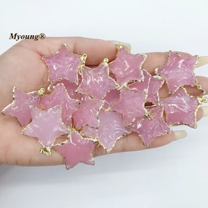 May include: A collection of pink star-shaped charms with gold-toned edges. The charms are made of resin and have a marbled effect. They are perfect for jewelry making or crafting.