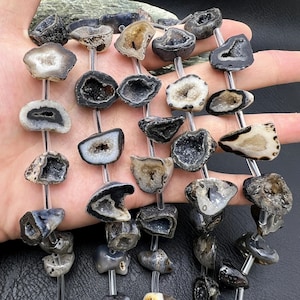 Peut inclure: Un collier de perles de pierres précieuses d'agate noir et blanc avec une finition druzy. Les perles sont de forme irrégulière et ont un aspect naturel et brut.