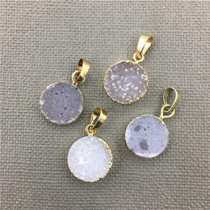 Puede incluir: Cuatro colgantes chapados en oro con rebanadas redondas de ágata blanca. El ágata tiene una textura natural, similar a la de un cristal.