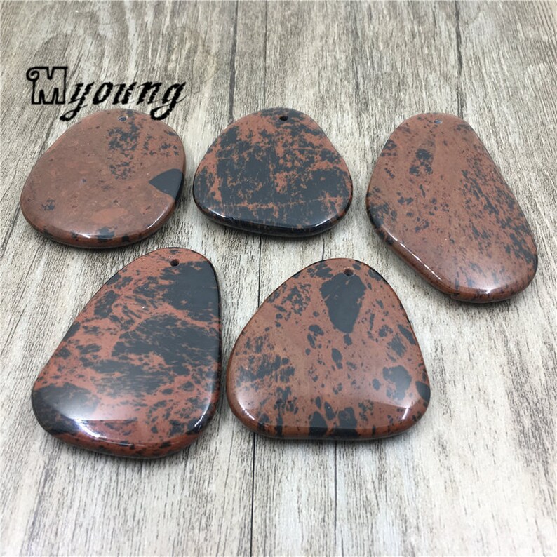 Puede incluir: Cinco colgantes de piedra moteados de marr&oacute;n y negro con un agujero perforado en la parte superior para colgar. Las piedras tienen una forma irregular y un acabado liso y pulido.