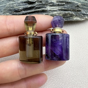 May include: Two small, square, crystal perfume bottles with gold stoppers and caps. The bottle on the left is clear with a smoky brown tint. The bottle on the right is a deep purple.