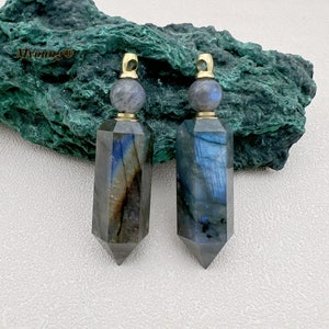 Peut inclure: Deux pendentifs en cristal de labradorite bleu irisé avec des embouts et des bélières dorés. Les pendentifs sont facetés et ont une pointe pointue. Ils sont présentés sur un fond de pierre verte.