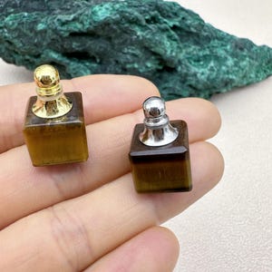 May include: Two small square bottles with gold and silver tops. The bottles are made of tiger's eye stone and have a brown and gold color.