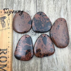Puede incluir: Cinco colgantes de piedra moteados de marr&oacute;n y negro con un agujero en la parte superior para encordar. Las piedras tienen una forma irregular y un acabado liso y pulido.