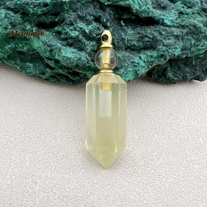 May include: A clear glass bottle pendant with a gold metal cap and a gold metal loop. The bottle is shaped like a crystal and has a pointed bottom. The bottle is filled with a clear liquid.
