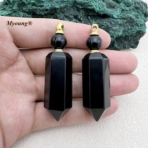 May include: Two black obsidian crystal bottle stoppers with gold caps and a gold loop for hanging. The stoppers are in the shape of a pointed, faceted crystal.