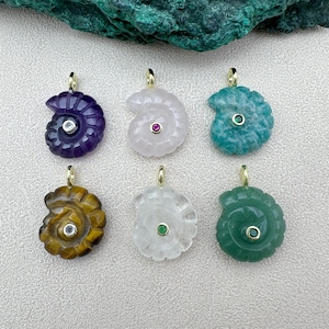 Pode incluir: Seis pingentes de pedras preciosas em forma de concha. Os pingentes são em várias cores, incluindo roxo, branco, verde-azulado, castanho, transparente e verde. Cada pingente tem uma fiança dourada e uma pequena gema no centro.