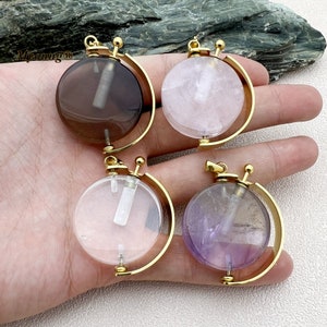 Może przedstawiać: Cztery złote zawieszki z okrągłymi, przezroczystymi kryształami. Każda zawieszka ma obracający się wzór globusa. Kamienie są przezroczyste, dymno-szare, różowe i fioletowe.