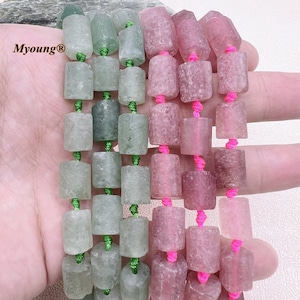 Peut inclure: Deux brins de perles, l'un vert et l'autre rose, sont enfilés sur un cordon avec du fil rose et vert. Les perles sont cylindriques et ont une surface rugueuse et texturée.